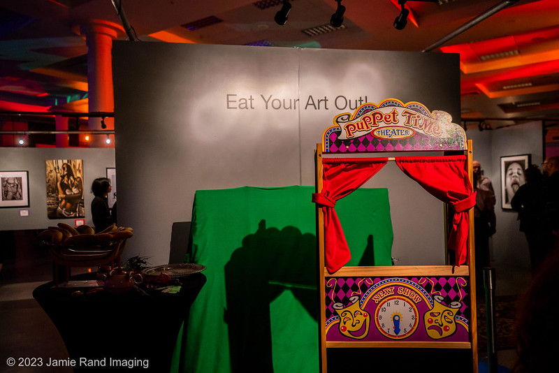 Interactive exhibit Eat Your Art Out - an unmanned puppet stage and green screen leaning against a gray wall. Exhibit was at the 2023 Seattle Erotic Art Festival.