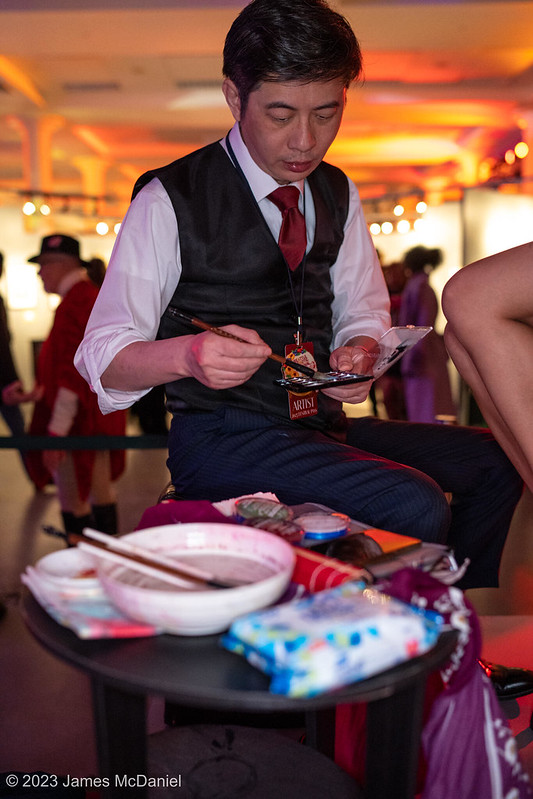 Artist sitting on stool mixing paints at the 2023 Seattle Erotic Art Festival