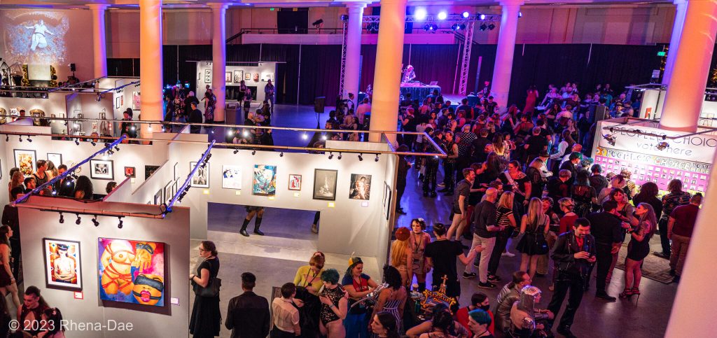 SEAF 2024 Saturday Schedule: View of the Seattle Center Exhibition Hall during the Seattle Erotic Art Festival 2023. Picture taken from balcony above stairwell, looking down on crowd and art walls.