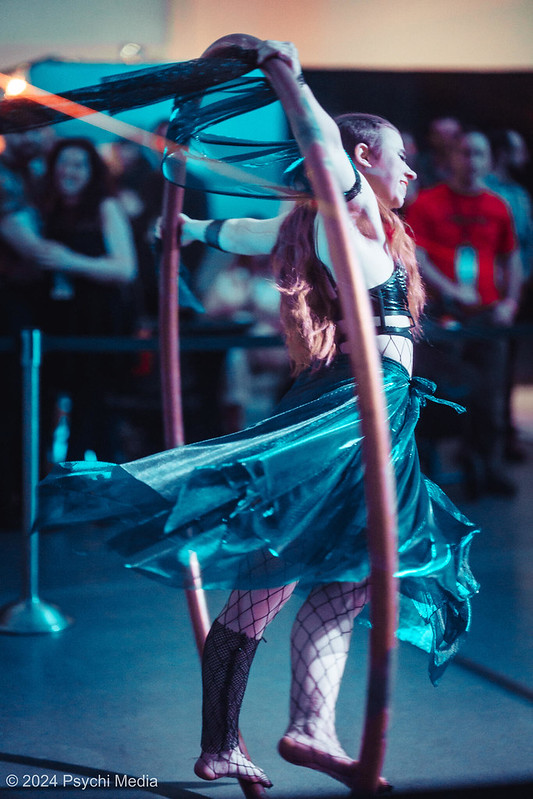 SEAF 2025 Call for Art: A woman, smiling, in a cyr wheel caught mid-motion, her skirt flying back behind her, while performing at the 2024 Seattle Erotic Art Festival.