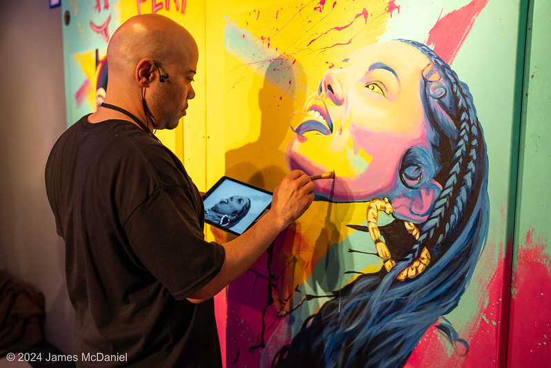 SEAF 2025 Call for Art: Artist Myron Curry painting a mural of a woman with long hair and large hoop earrings at the 2024 Seattle Erotic Art Festival.