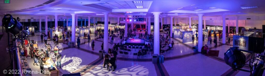 2025 Visual Artists: A panoramic pictures of the 2022 Seattle Erotic Art Festival from above the bar, showing a atmospherically lit view of the Seattle Center Exhibition Hall.